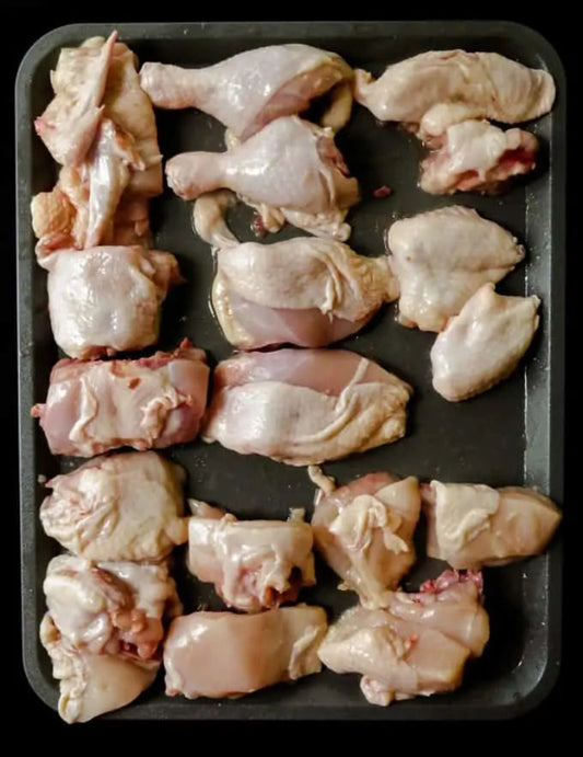 Raw chicken pieces on a black tray. Raw, high-quality free-range Naadan Kozhi and Desi chicken pieces, showcasing firm meat texture and authentic natural fat trim, prepared fresh on a clean cutting surface.